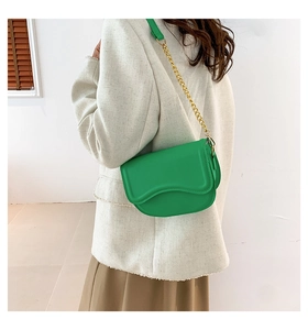 Detail of a bright green saddle bag featuring a gold chain strap and smooth matte leather