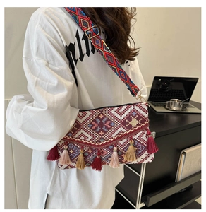 Macro view of ethnic knit crossbody bag featuring colorful tassels and wide woven strap