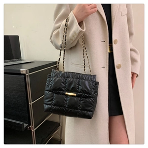 Detail of black quilted shoulder bag featuring glossy finish and gold chain strap