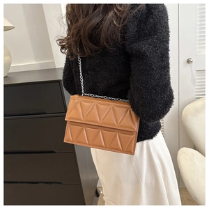Detail view of brown quilted crossbody bag with silver chain strap on model's shoulder