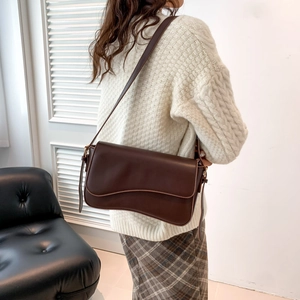 Deep brown crossbody flap bag with wavy lid design shown on model for autumn fashion
