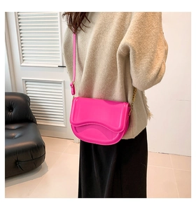 Detail of hot pink glossy saddle bag with wavy flap and gold chain strap on model