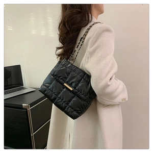 Modern black quilted down shoulder bag with gold metal clasp on a beige coat model
