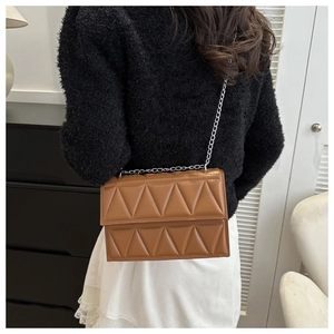 Close-up of brown quilted faux leather crossbody bag with silver chain on model