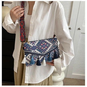 Detail of bohemian knit crossbody bag featuring colorful geometric embroidery and blue tassels