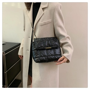 Detail of black quilted puffer shoulder bag featuring a gold chain and metallic buckle