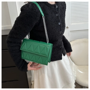 Detail showing the green quilted crossbody bag with silver chain strap on a model