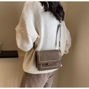 Close-up of brown leather crossbody bag with white contrast stitching and ethnic strap