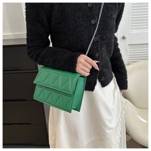 Detail of green quilted crossbody bag with silver chain strap on a model wearing black