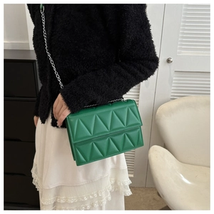 Detail of green quilted shoulder bag with silver chain worn by model for casual style