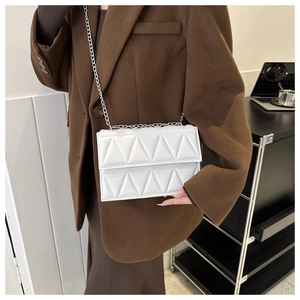 Close-up of white geometric quilted crossbody bag with silver chain on brown wool coat