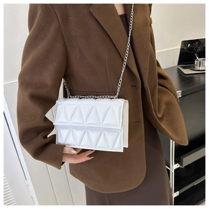 Close-up of white quilted crossbody bag with silver chain strap on an office desk