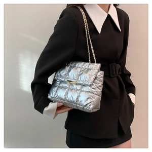 Close-up of silver quilted chain bag with gold metal clasp on a black coat outfit
