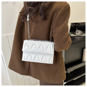 Close-up of a white quilted crossbody bag with a silver chain strap worn with a brown coat