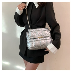 Detail view of silver quilted shoulder bag with golden lock and chain strap for women