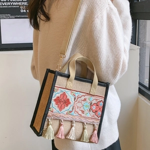 Detail of ethnic embroidery and soft fringe tassels on a beige canvas crossbody bag