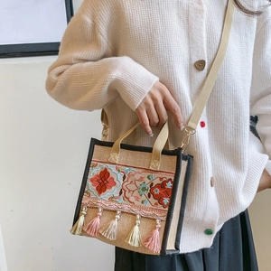 Close-up of ethnic embroidery and colorful tassel charms on a textured canvas tote bag