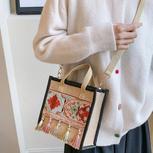 Detailed close-up of ethnic embroidery and colorful tassels on the beige canvas handbag