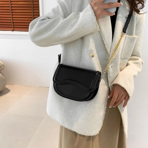 Minimalist black saddle bag with wave-curve flap and gold chain strap on model