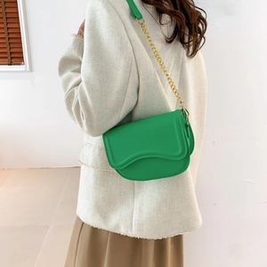 Green leather saddle bag with gold chain strap shown on model in a minimalist setting