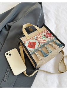 Ethnic jute tote bag with floral embroidery and tassels shown on a white fabric background