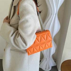Chic orange quilted crossbody bag with silver chain strap worn over a beige coat