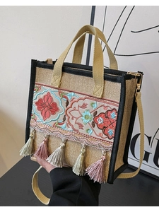 Ethnic straw tote bag with multi-color floral embroidery and long tassels in hand-held view