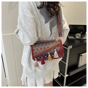 Détail d'un sac bandoulière bohème tissé avec motifs ethniques et pompons colorés