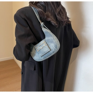 Detail of light blue denim crescent shoulder bag with metallic buckle on black coat