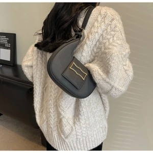 Détail du sac hobo en cuir noir avec boucle dorée porté sur un pull en maille beige
