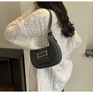 Detail of a black half-moon shoulder bag with a vintage gold buckle on a knit sweater