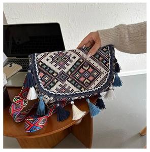 Détail du sac tissé bohème avec broderies colorées à pompons et large bandoulière