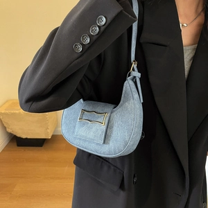 Sac hobo demi-lune bleu clair avec boucle dorée porté par un mannequin en tailleur noir