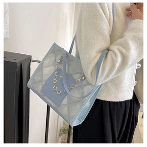 Detailed macro view of quilted blue tote bag featuring a decorative gold flower metal chain