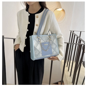 Detail of light blue quilted tote bag with gold chain and fashion text on model
