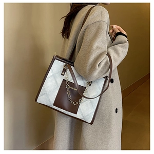 Detail of grey checkered tote bag with brown straps and golden floral chain accents