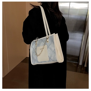 Detailed view of light blue denim tote bag with chain strap worn on a black coat