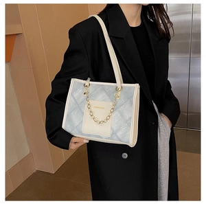 Detail of blue quilted denim tote bag with white leather trim and gold chain ornament
