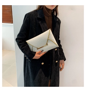 Dettaglio di pochette a busta bianca intrecciata con finiture in metallo dorato e chiusura