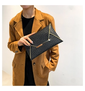 Dettaglio pochette nera intrecciata con finiture in metallo dorato e patta a busta