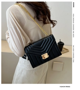 Close-up of black quilted shoulder bag with V-shaped pattern and gold metal chain strap
