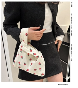Detail view of white corduroy tote bag with red strawberry pattern held by a model