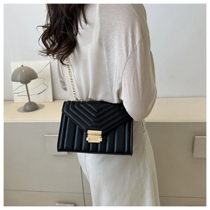 Chic black quilted shoulder bag with gold chain strap worn over a white outfit