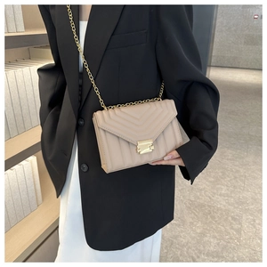 Detail of a beige quilted envelope crossbody bag with a slim gold chain and V-pattern