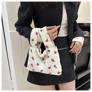 Detailed view of cream corduroy handbag with red strawberry print held by a model