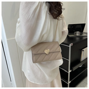 Detail of beige quilted crossbody bag with golden heart clasp and chain strap