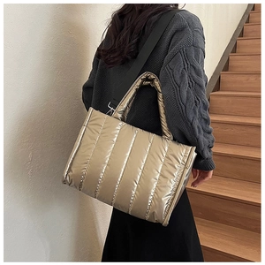 Golden quilted tote bag shown on stairs with puffer texture and wide shoulder strap