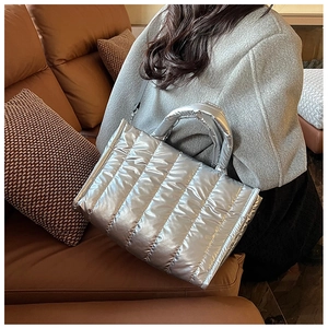 Detail of silver quilted puffer bag on sofa showing glossy texture and strap