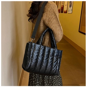 Close-up of black quilted puffer tote bag with glossy finish and wide shoulder strap