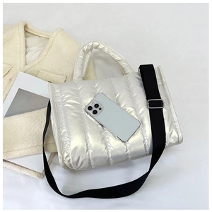 Close-up of metallic quilted puffer bag with crossbody strap and size reference phone